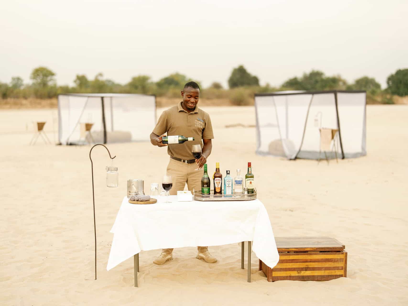 Sleep_under_The_Stars_Time_&_Tide_Luwi_©_Oliver_Fly_Photography_3-A server pouring wine at the bar setup at the sleepout under the stars with Time + Tide in Zambia