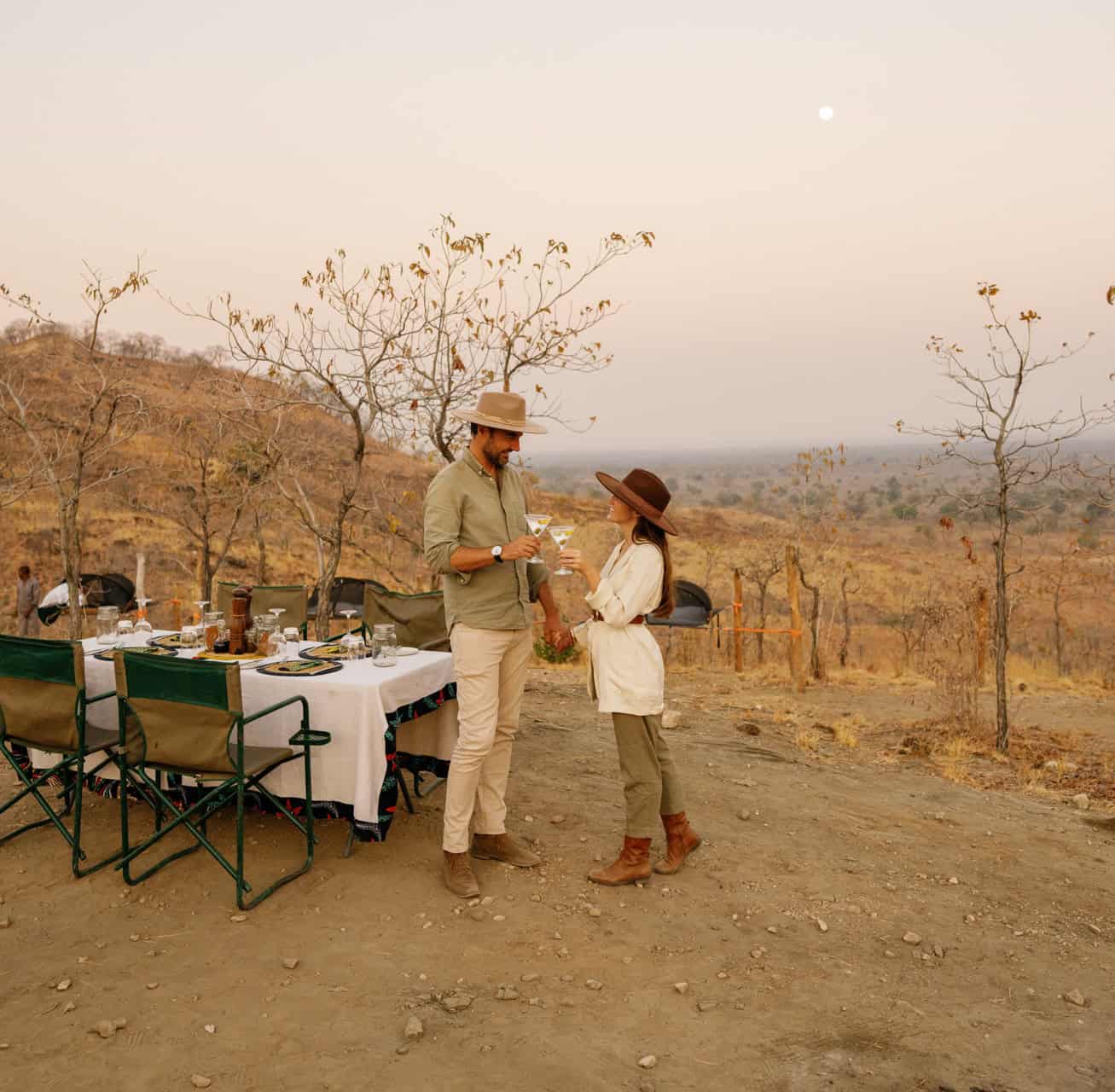 Sleepout_Under_The_Stars_Chongwe_Time+Tide_©_Oliver_Fly_Photography_433-Two guests holding up their drinks on a bush dinner with Time + Tide in Zambia