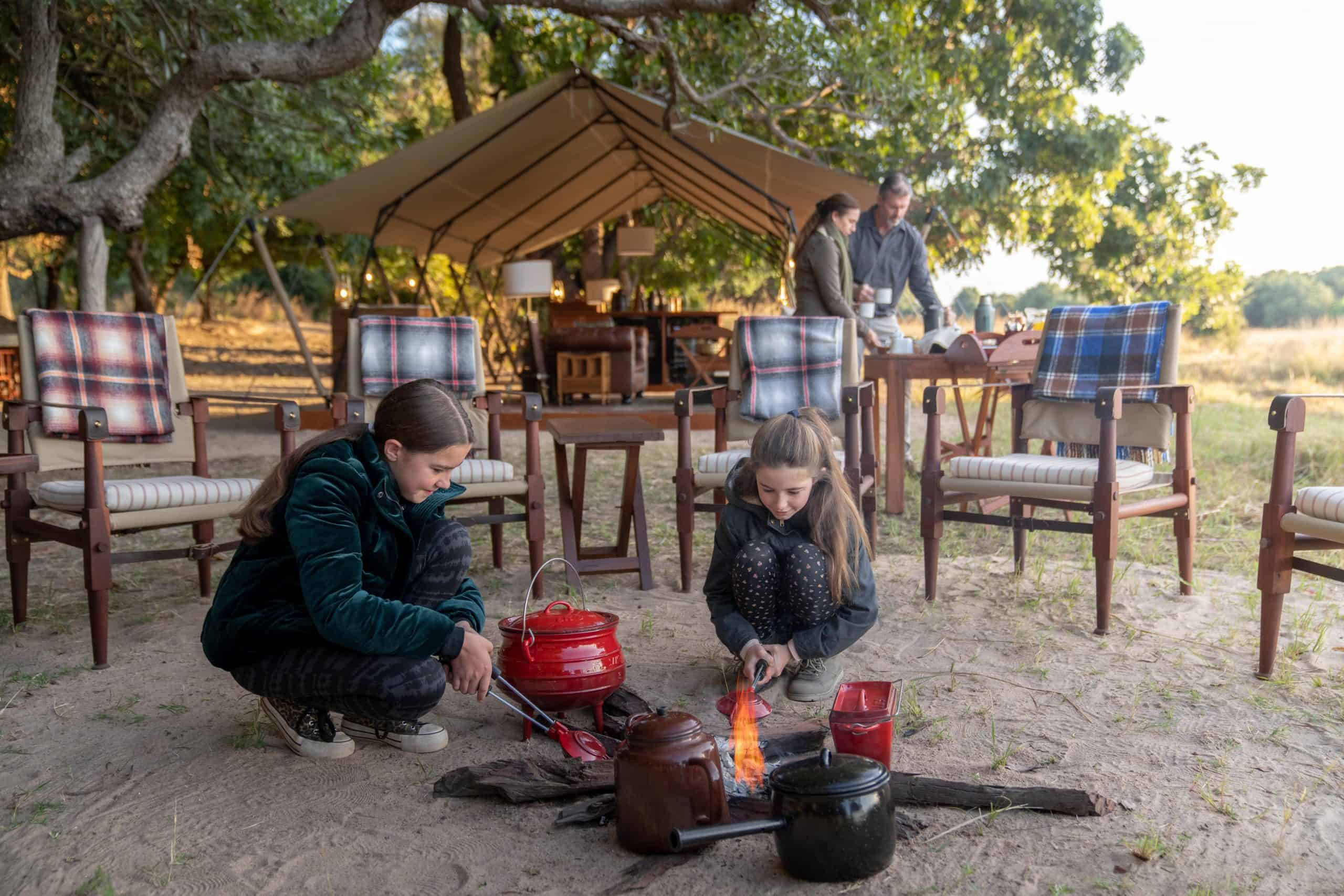 Children kneeling next to the fire pit warming food at Time + Tide Luwi Camp in teh South Luangwa Zambia