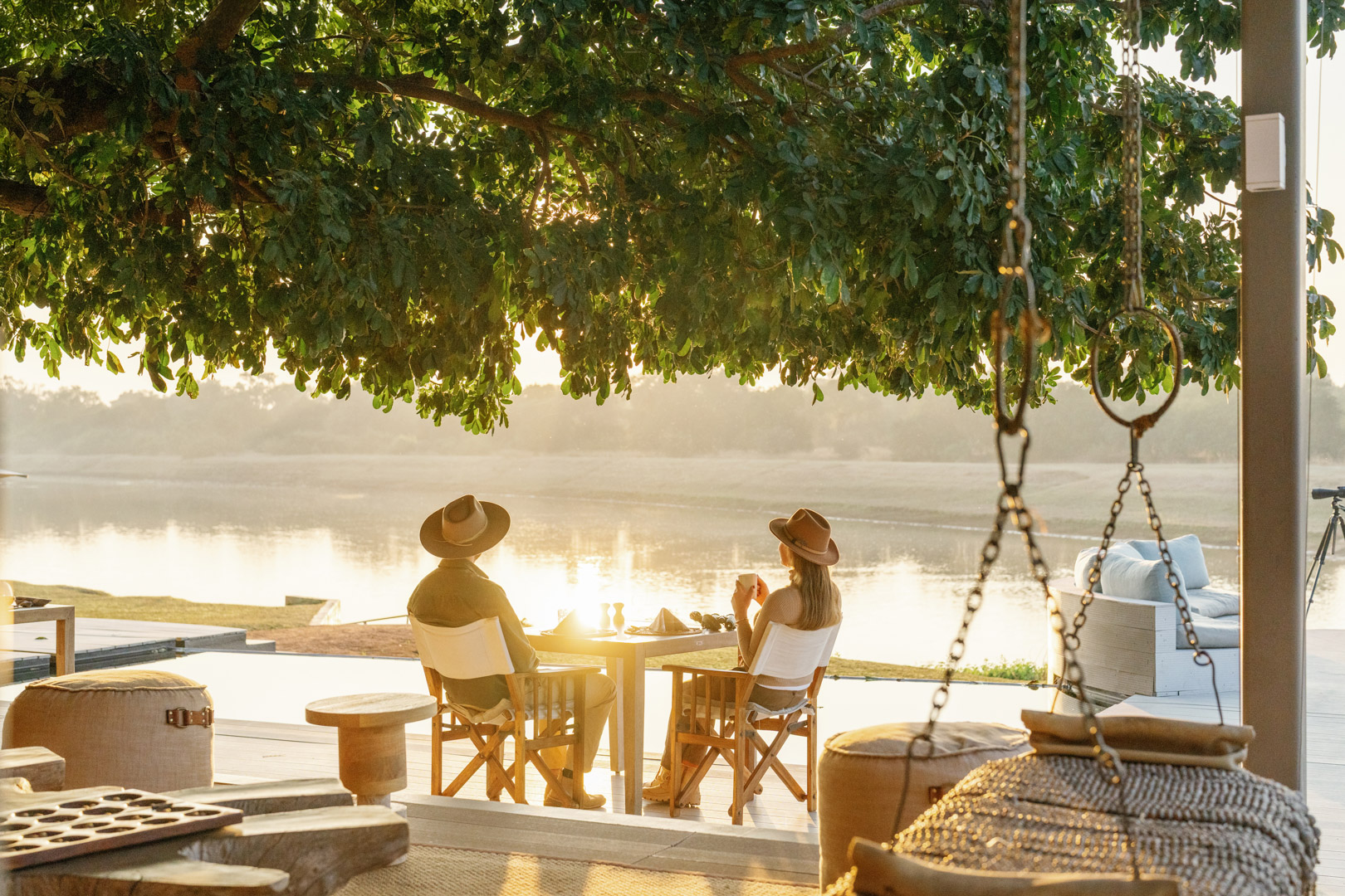 Two guests sitting at a table, drinking coffee, overlooking the river and watching the sun rise on safari in Zambia
