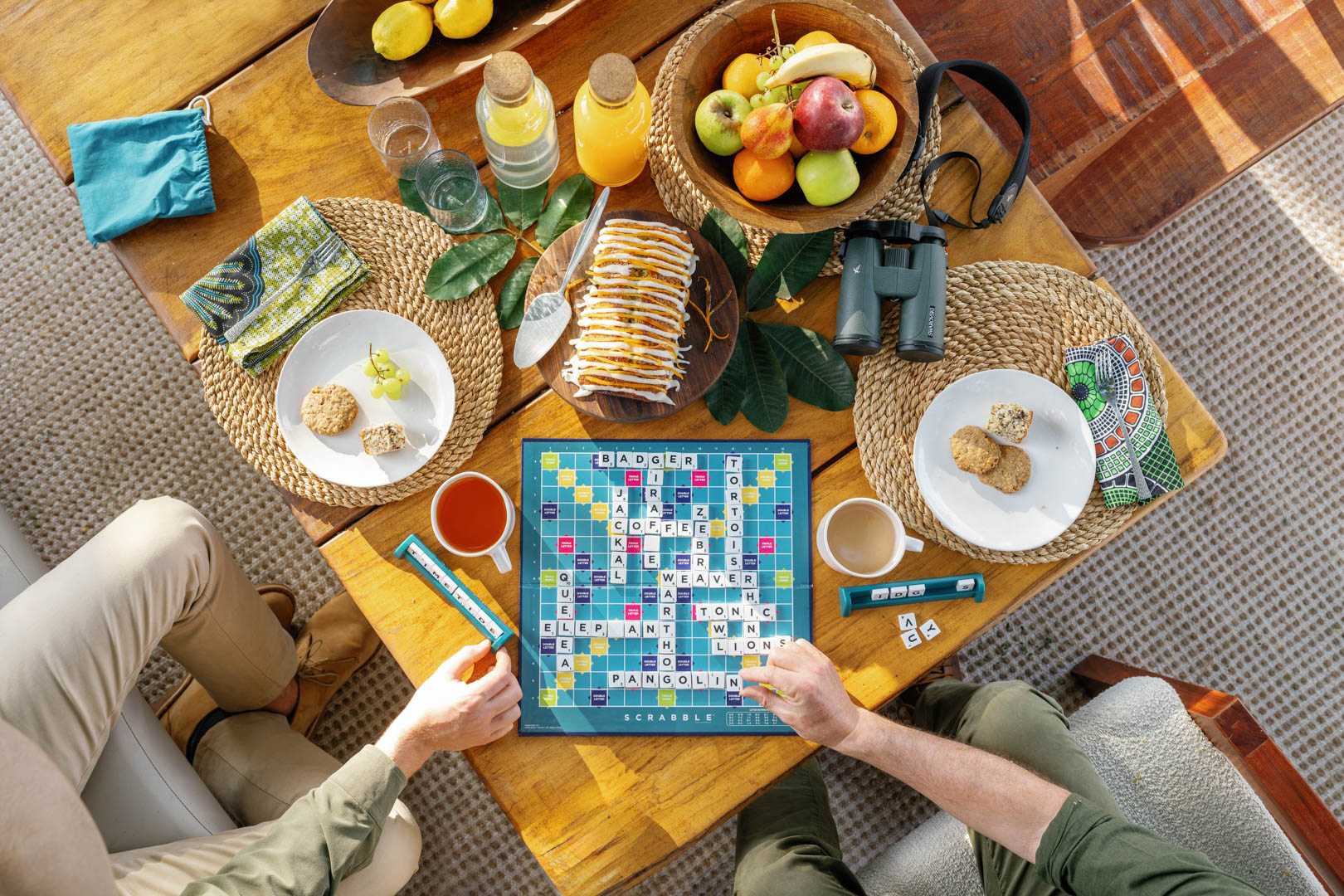 Birdseye view of two guests playing scrabble at tea time with Time + Tide Safaris in Zambia